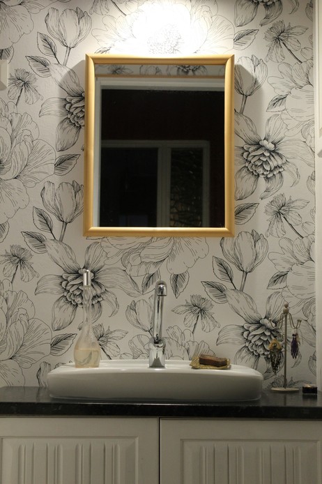 Lavabo con specchio dalla cornice dorata su parete rivestita da carta da parati a fiori disegnati in bianco e nero