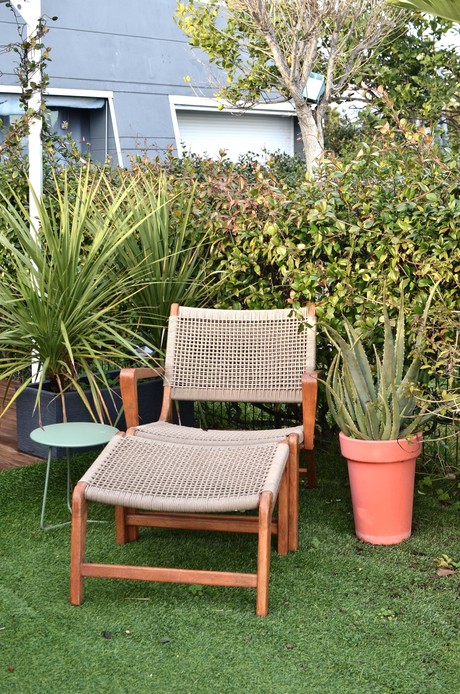 Poltrona con struttura in legno e seduta in corda intrecciata, affiancata da poggiapiedi e vaso in terracotta con aloe