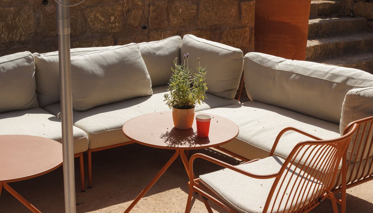 Salotto da giardino in polyrattan intrecciato con divano, due poltrone tonde e tavolino, cuscini beige, su un patio con piante
