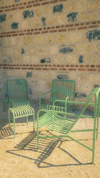 Tre sedie da giardino in tubo di metallo verniciato verde davanti a un muro in pietra e mattoni, con ombre nette a terra
