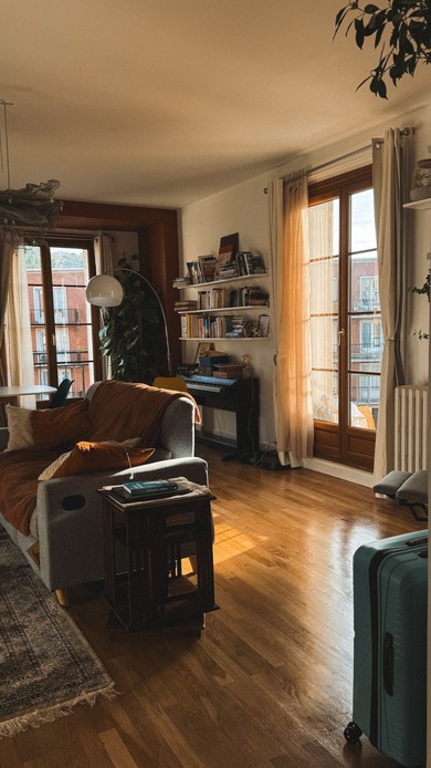 Soggiorno accogliente con luce dorata che filtra da porte a vetri con tende in lino, libreria e divano con plaid color ruggine