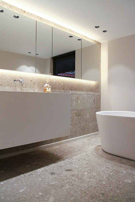 Specchio a tutta larghezza sopra il lavabo in un bagno rivestito in pietra, con vasca freestanding bianca