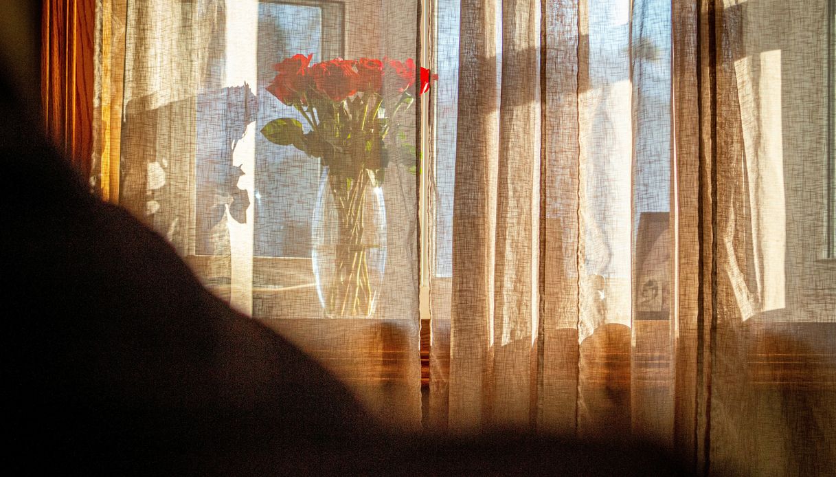 Tenda in lino leggero controluce con un vaso di rose rosse visibile in trasparenza sullo sfondo