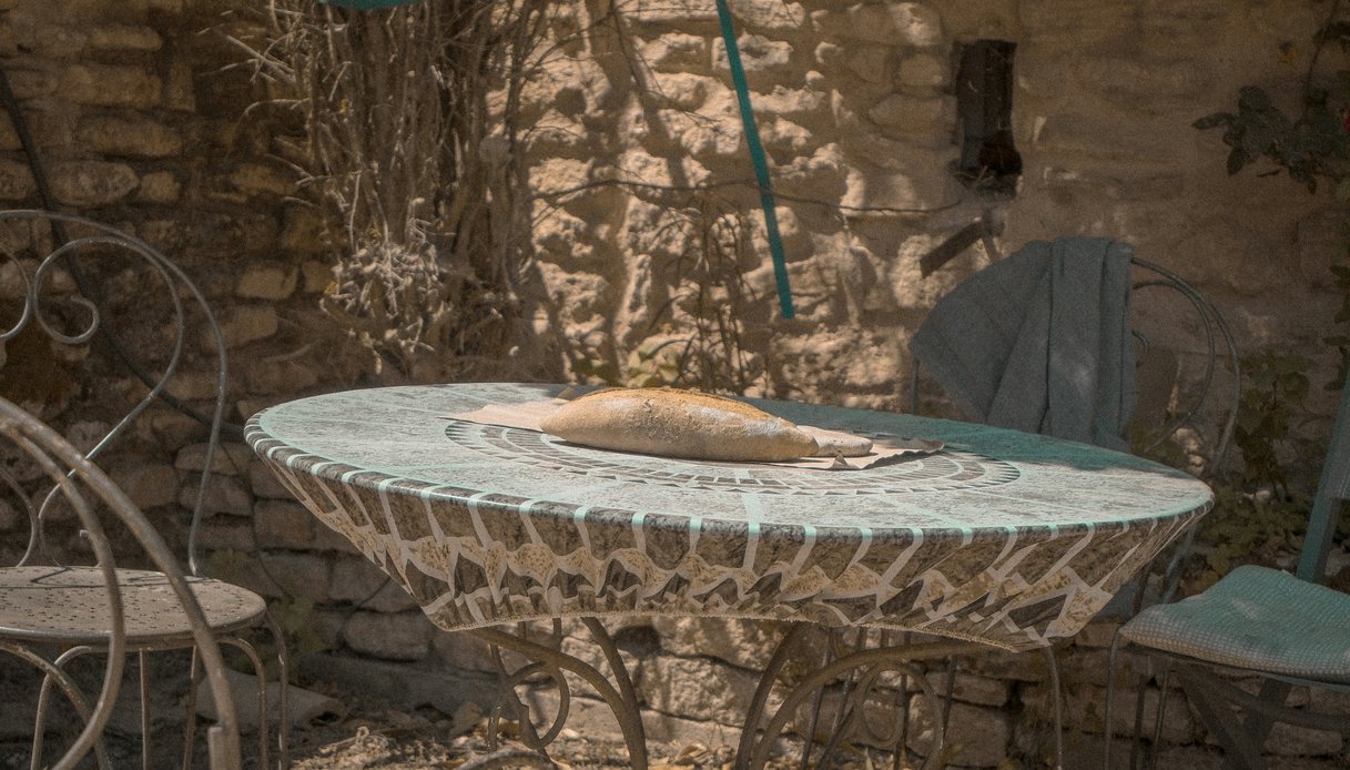 Tavolo tondo in mosaico e sedie in ferro battuto in un cortile di pietra, con pane appoggiato al centro