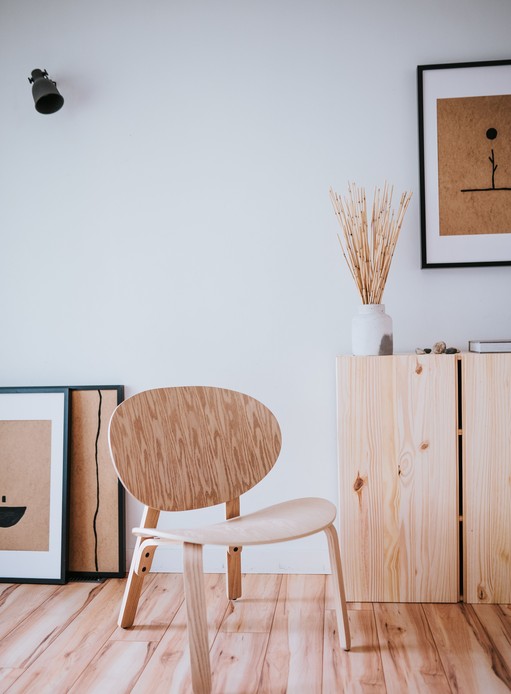 Angolo minimalista con sedia in legno curvato, mobili in pino chiaro, stampe su cartone e pavimento in legno chiaro