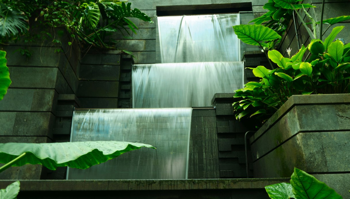 Cascate a gradoni d'acqua che scendono lungo pareti in pietra scura, circondate da fitta vegetazione tropicale