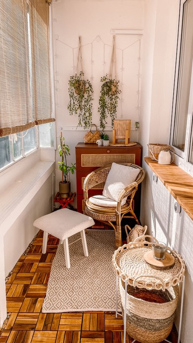 Piccolo balcone boho con tappeto in juta a rombi, sedia in rattan, sgabello in boucl&eacute; e portavasi in macram&egrave; con piante ricadenti alla parete