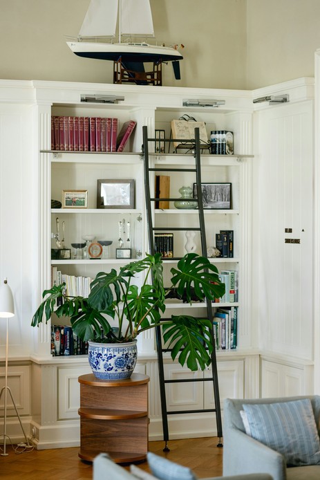 Libreria a boiserie bianca con modellino di veliero in cima, libri e una grande giara in ceramica bianca e blu su un supporto in legno.