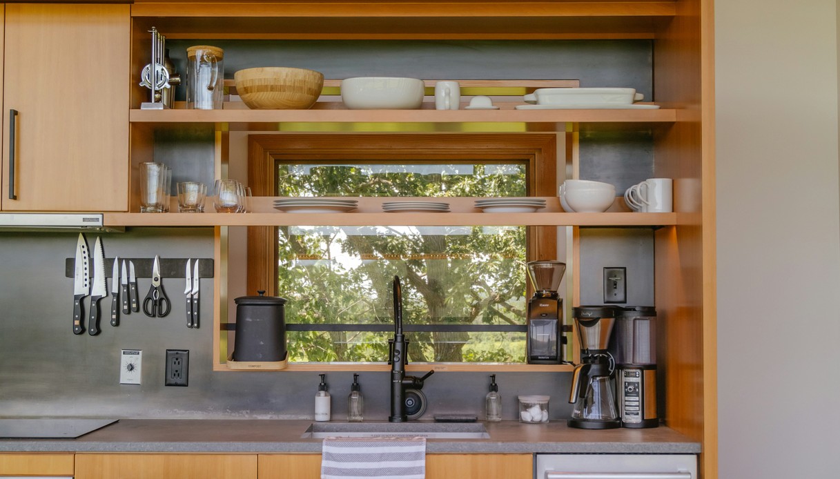Cucina in legno con mensole a vista e piccola finestra passavivande sopra il lavello