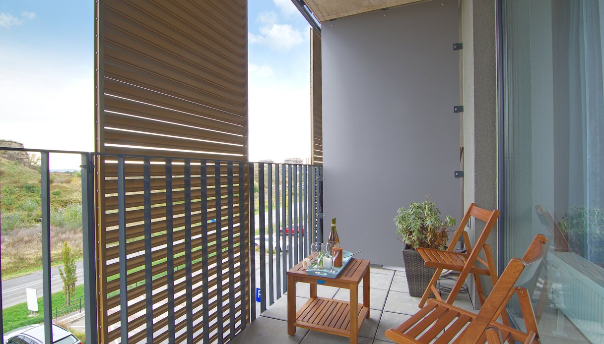 Balcone con pannello frangisole a doghe di legno su un lato, tavolino e sedie pieghevoli in legno