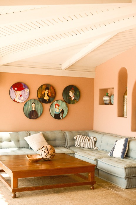 Cinque piatti tondi in ceramica con ritratti femminili dipinti, disposti su una parete color terracotta sopra un divano.