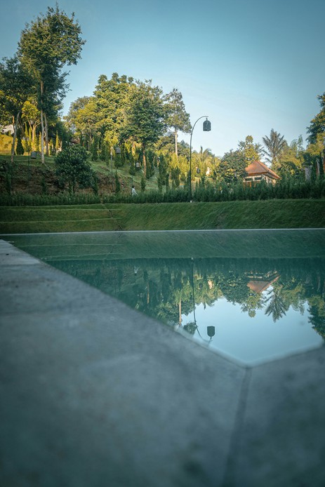 Piscina a specchio al crepuscolo che riflette alberi, cielo e un giardino terrazzato in collina