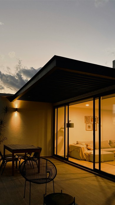 Terrazza al tramonto con sedia nera e luci calde che escono dalle vetrate