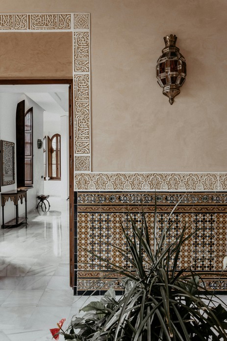 Parete di un interno marocchino con zoccolatura in zellige a stella, stucchi intagliati e una lanterna in vetro colorato.