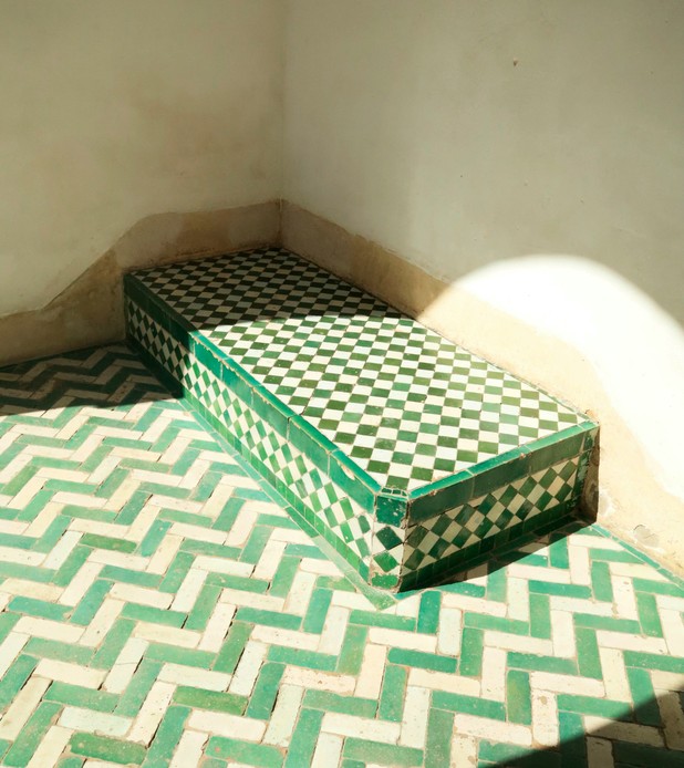 Panca rivestita in zellige verde e bianco a scacchi, con pavimento a spina di pesce verde, illuminata da un raggio di sole.