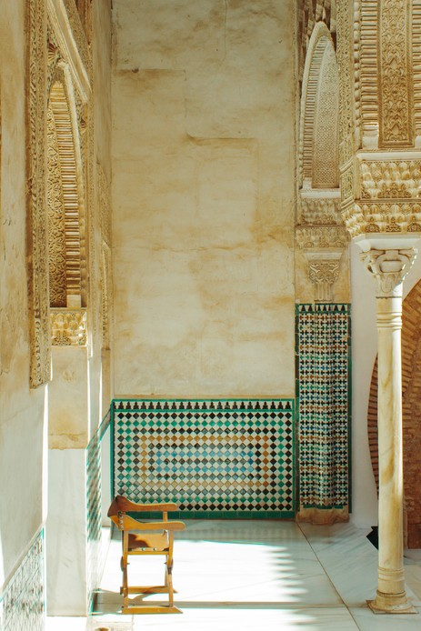 Zoccolatura in mosaico di zellige verde, blu e ocra alla base di una parete in un palazzo moresco, accanto a una colonna in marmo.