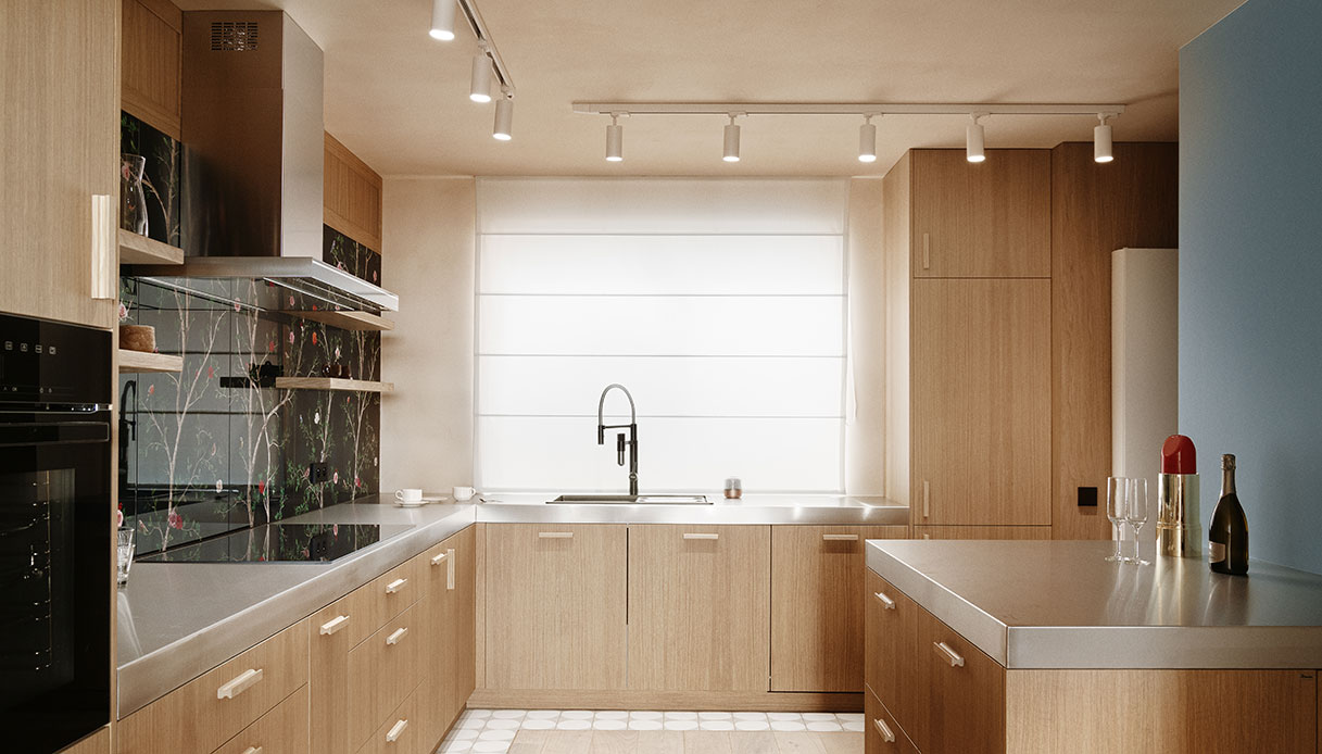 Cucina in rovere con piani in acciaio inox e rivestimento in piastrelle a motivo floreale su fondo scuro