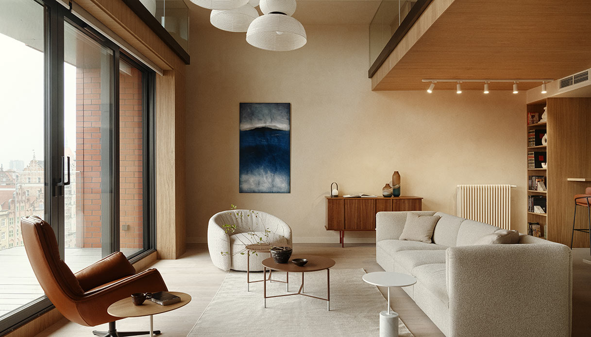 Zona salotto con divano chiaro, poltrona girevole in pelle cognac e credenza in legno scuro