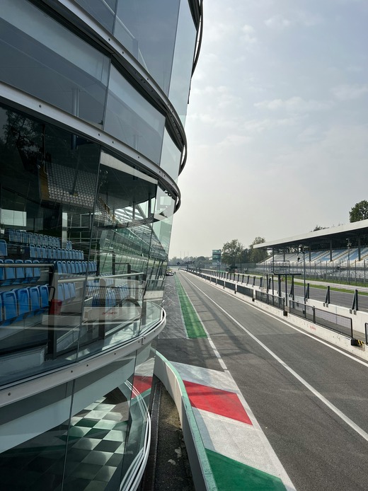La parete vetrata inclinata della palazzina box dell'Autodromo di Monza vista dalla corsia dei box, con le tribune riflesse nel vetro