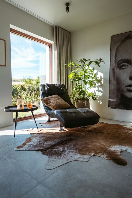 Chaise longue in pelle nera su base cromata accanto a una grande vetrata in soggiorno