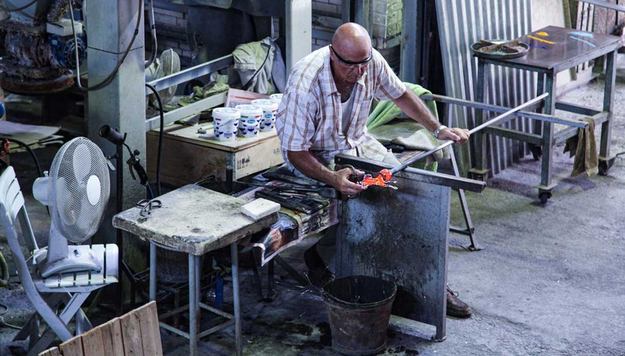 Maestro vetraio al lavoro in fornace su una massa di vetro incandescente