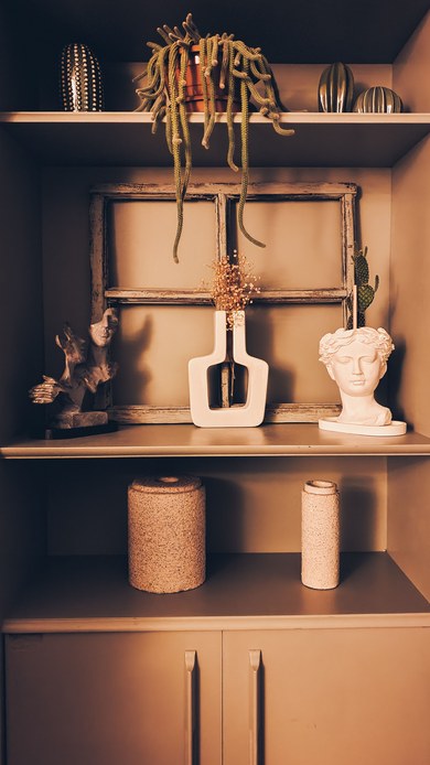 Mensole con cactus ricadente in vaso di terracotta, vasi in ceramica dalle forme organiche, oggetti in sughero e un vaso a forma di testa classica