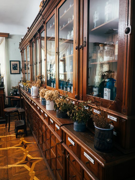 Grande vetrina antica in legno con vasi e flaconi di vetro, base a cassetti con etichette smaltate e vasi di fiori secchi sul piano
