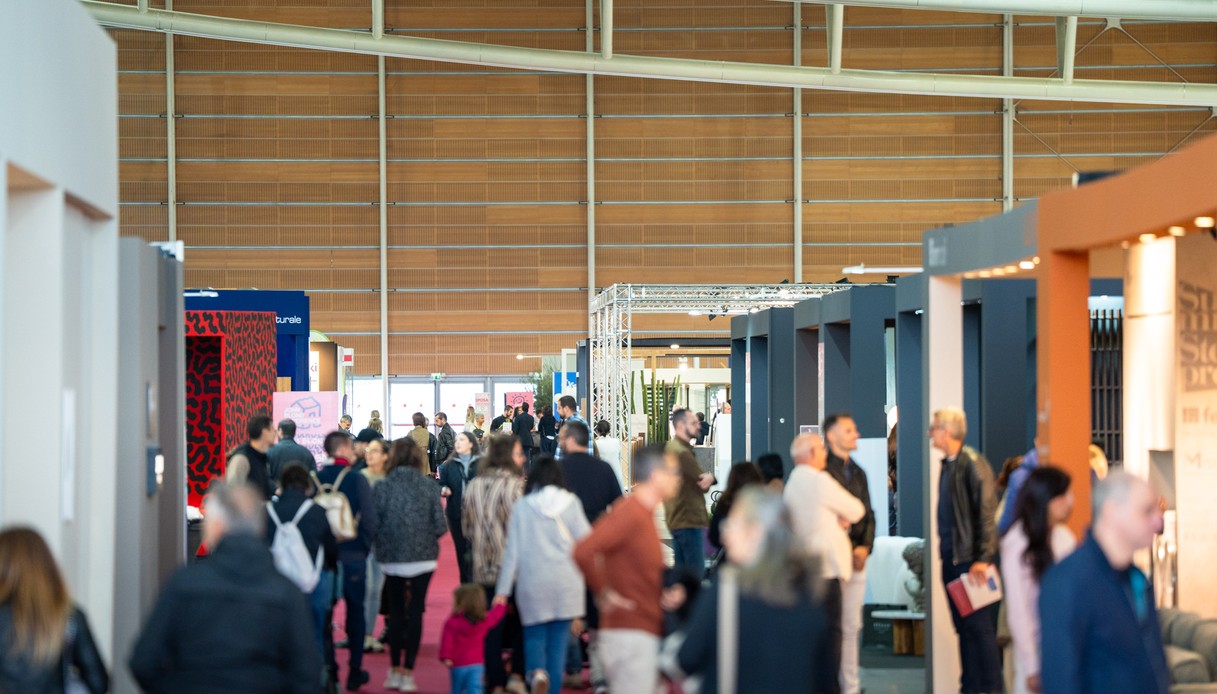 Visitatori lungo una corsia con moquette rossa tra gli stand espositivi dell'Oval Lingotto, con la grande parete in legno del padiglione sullo sfondo