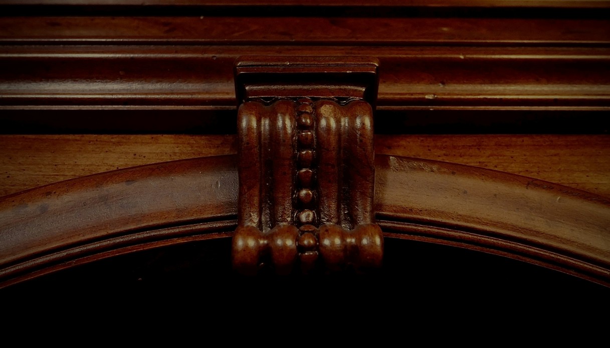 Primo piano di una mensola intagliata in legno di noce con motivo a perline al centro di un arco decorato