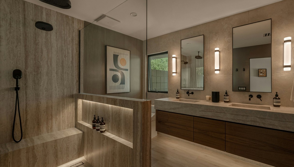 Bagno in travertino con doccia aperta, panca in muratura, nicchia illuminata, rubinetteria nera, doppio lavabo con mobile in legno e specchi rettangolari