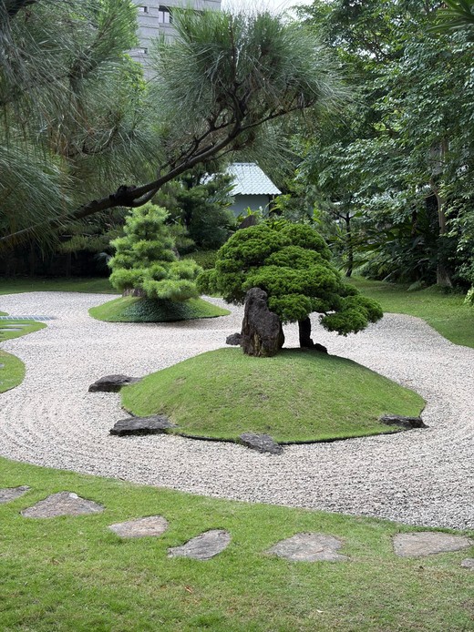 Giardino giapponese con ghiaia chiara rastrellata, isole erbose con pini potati e rocce, e passi in pietra immersi nel prato