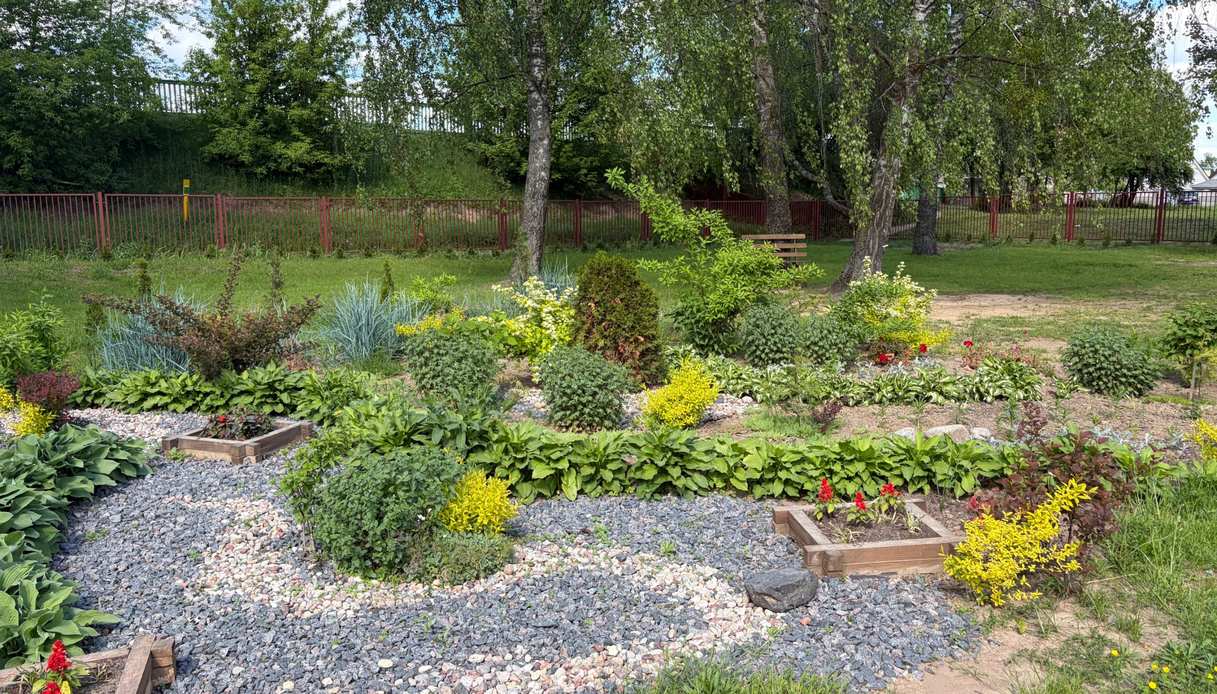 Giardino con grandi rocce calcaree traforate, arbusti potati a sfera, aceri rossi e aiuole fiorite bordate in legno su una pavimentazione in pietra