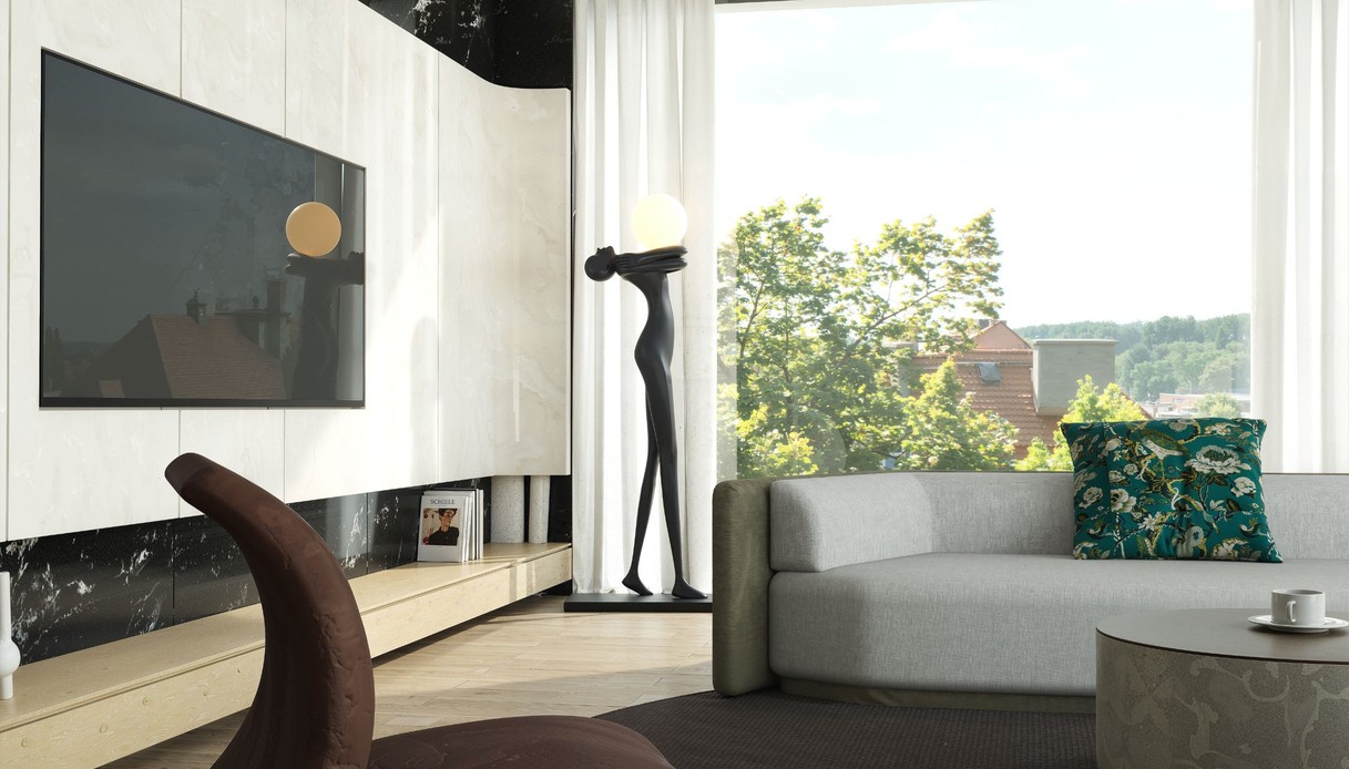Lampada da terra a forma di figura femminile stilizzata nera che sorregge una sfera luminosa, accanto a una grande finestra con vista sugli alberi, divano grigio e parete attrezzata in marmo chiaro e nero