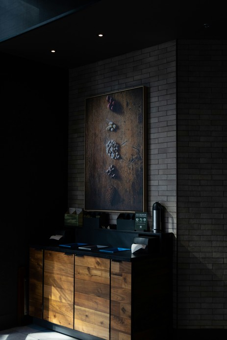 Mobile basso con ante in legno di noce dalle venature evidenti, piano nero e parete in mattoncini scuri con quadro