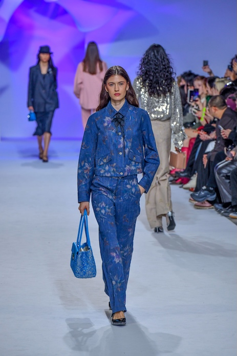 Modella alla sfilata Shiatzy Chen durante la Paris Fashion Week con completo denim blu scuro decorato da motivi floreali e fiocco nero al collo.