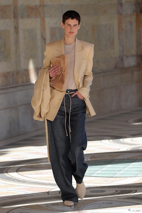 Modella alla sfilata Gabriela Hearst durante la Paris Fashion Week con blazer beige, maglia chiara e jeans blu scuro a gamba ampia.