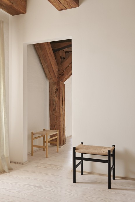 Due sgabelli CH53 di Hans J. Wegner, uno in rovere naturale e uno in legno laccato nero, con seduta in corda di carta intrecciata, in un ambiente bianco con travi e pilastro in legno antico